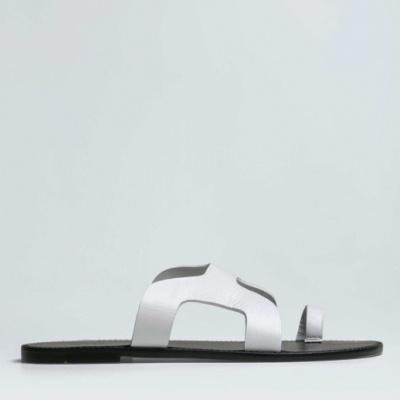 Sandália rasa preta com tiras brancas de pele, estilo chinelo, sobre fundo cinza claro.