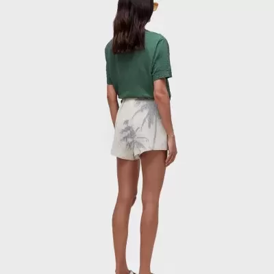 Mulher de costas com t-shirt verde, calções brancos com padrão de palmeiras e sandálias brancas