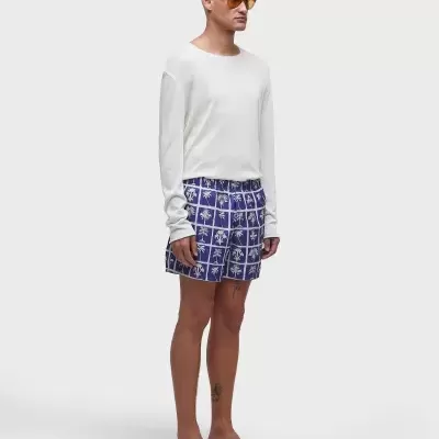 Pessoa com camisola branca, calções azul com padrão branco e chinelos pretos
