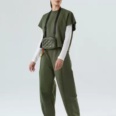 Mulher a usar t-shirt verde oliva, camisola branca, calças largas verdes, sapatilhas brancas e bolsa matelassé verde com alça preta