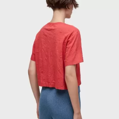 T-shirt vermelha de manga curta com textura enrugada vista de costas e calças azuis de malha.