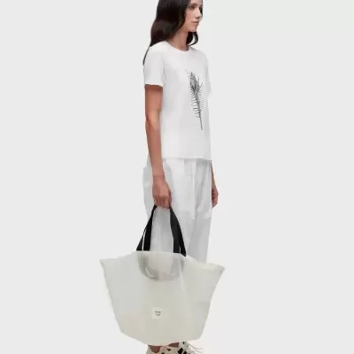 Mulher com roupa branca e bolsa branca translúcida com alças pretas