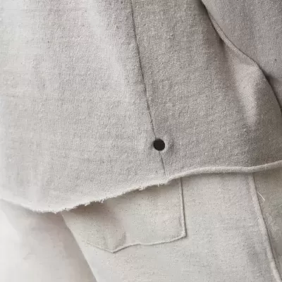 Detalhe de roupa bege clara em tecido de algodão ou linho com botão preto e bolso.