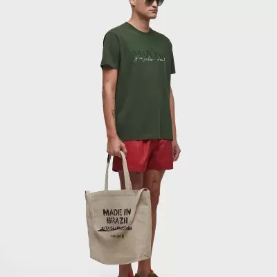 Homem com t-shirt verde e calções vermelhos segurando sacola com texto Madeira in Brazil