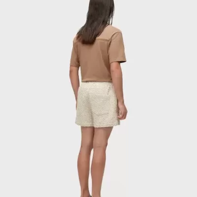 Pessoa de costas com camisola bege castanha e calções brancos texturizados.