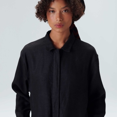 Mulher a usar camisa preta de manga comprida e lenço colorido na cabeça, fundo cinza claro