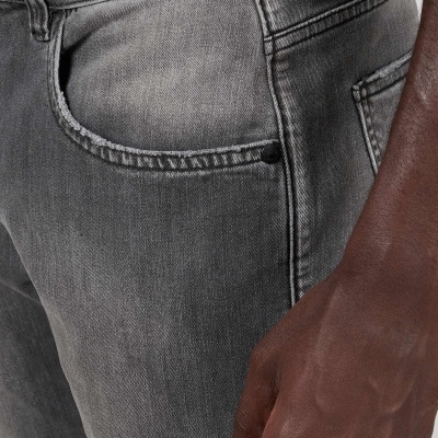 Calças de ganga cinzentas com bolsos e botão negro, detalhe de mão encostada.