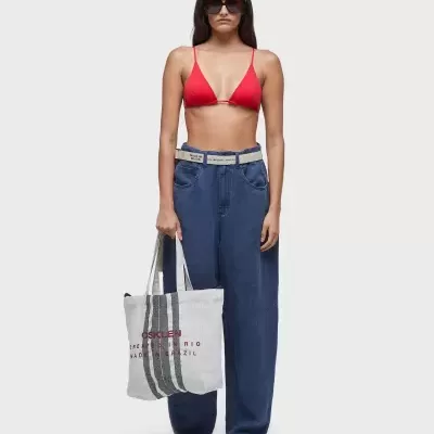 Mulher com roupa casual e bolsa de pano branca com texto em fundo cinzento