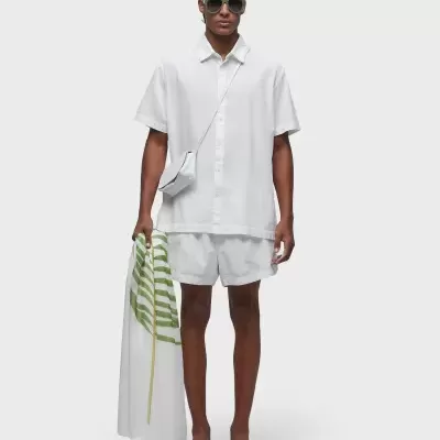 Homem vestido com roupa casual branca e acessórios segurar pano com folha verde.