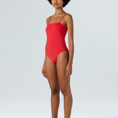 Mulher com fato de banho vermelho e sandálias pretas em fundo cinzento claro