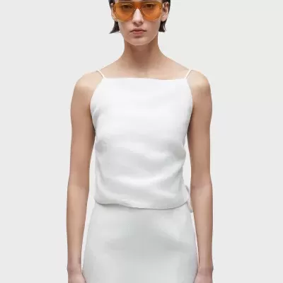 Mulher com vestido branco e óculos de sol amarelos em fundo cinza.