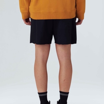 Pessoa vista de costas com sweat laranja, bermuda preta e sapatilhas pretas em fundo branco