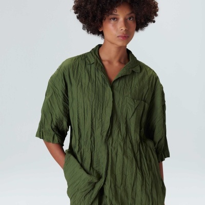 Camisa verde-oliva com textura vincada e bolso no peito usada com calções iguais.