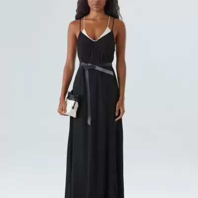 Mulher com vestido comprido preto e mala pequena branca e preta