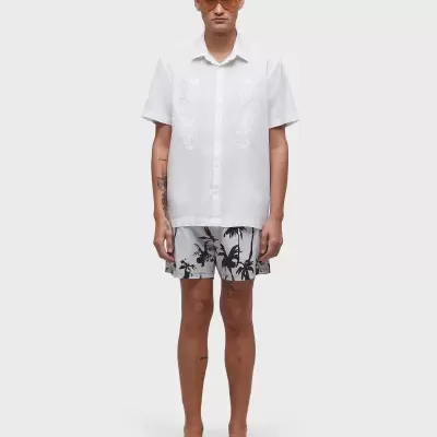 Homem com camisa branca e calções cinza com padrão de folhas em fundo branco