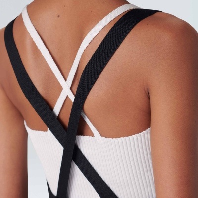 Costas de pessoa a vestir peça com alças cruzadas pretas e brancas, detalhe de tecido canelado branco.