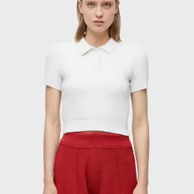 Mulher com camisola cropped branca de malha com gola e calças largas vermelhas texturizadas sobre fundo neutro