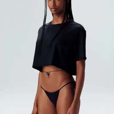 Mulher com top preto e tanga preta em fundo cinza claro