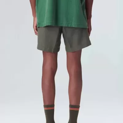 Homem de costas a usar t-shirt verde, calções cinza escuro, meias verdes e sapatos pretos