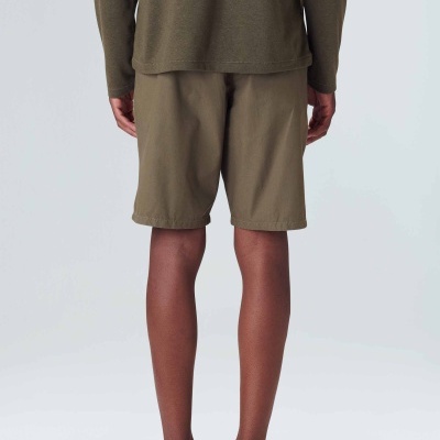 Homem visto de costas com roupa casual verde-oliva e verde-kaki em fundo cinzento.