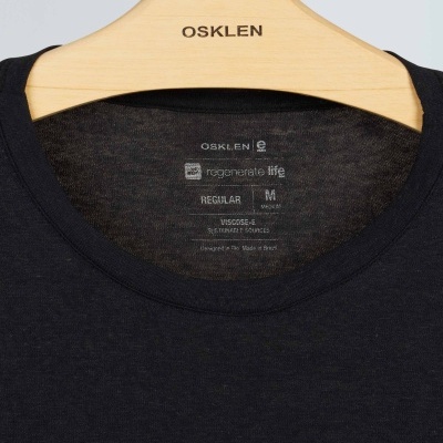 T-shirt preta com etiqueta interna pendurada em cabide de madeira OSKLEN