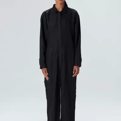 Mulher vestindo macacão preto de manga comprida com fundo cinza claro