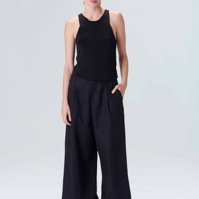 Mulher com regata preta e calças largas pretas em fundo cinzento