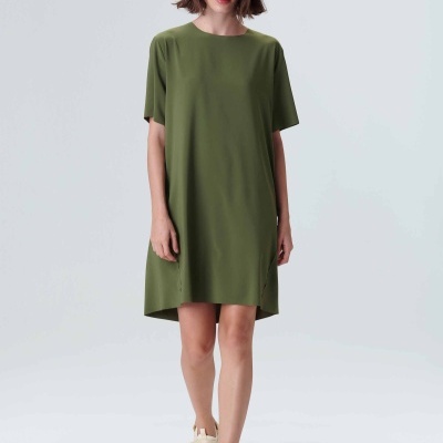 Mulher com vestido verde escuro, chapéu verde e sandálias bege, em fundo branco.