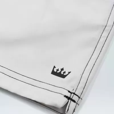 Peça de roupa branca com costuras pretas e símbolo de coroa preta próximo à bainha