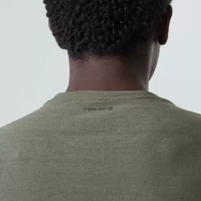 Pessoa com cabelo encaracolado vestindo t-shirt verde oliva com texto C.P. COMPANY na parte de trás.