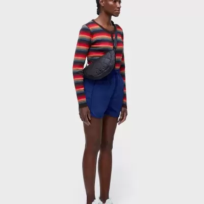 Mulher com camisola às riscas, calções azuis, sapatilhas brancas e bolsa preta pochete