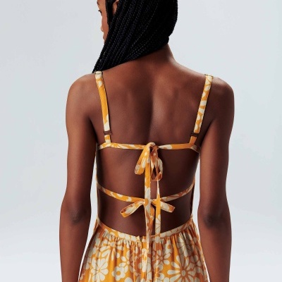 Modelo de costas a usar vestido amarelo com padrão floral branco e tiras ajustáveis amarradas.