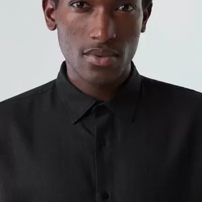 Homem a usar camisa preta de tecido liso com colarinho clássico e botões pretos