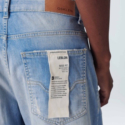 Calças de ganga azuis claras com etiqueta branca no bolso traseiro e etiqueta castanha na cintura com a palavra OSKLEN