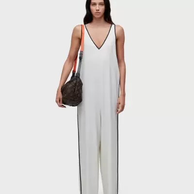 Macacão branco com decote em V e mala de couro castanha com alça vermelha e preta.