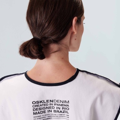 Pessoa vista de costas com t-shirt branca com bordas pretas e texto impresso nas costas.