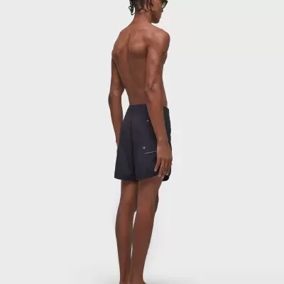 Homem de perfil com calções de banho pretos, chinelos pretos e óculos de sol