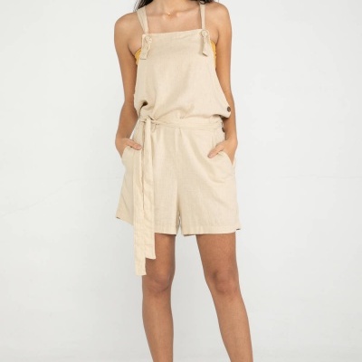 Macacão curto bege com cinto e alças finas, sapatos amarelos, modelo em fundo branco