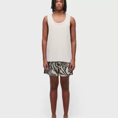 Homem com camisola branca, calções estampados e chinelos pretos em fundo branco