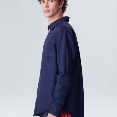 Homem veste camisa azul escuro de algodão com bolso no peito em fundo neutro.