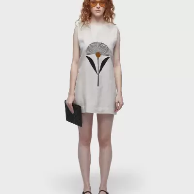 Vestido branco com estampa de flor estilizada, mulher com carteira preta e óculos laranja