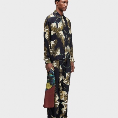 Homem a usar pijama floral preto com camisa de botões e calças largas, segurando lenço colorido.