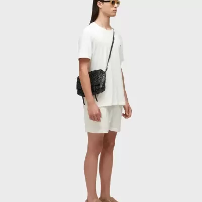 Pessoa com roupa branca, sapatos castanhos e bolsa preta trançada