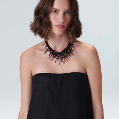 Colar preto com espinhos usado por mulher com vestido preto sem alças