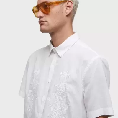 Camisa branca bordada de manga curta com botões usada por modelo com óculos de sol