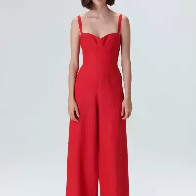 Macacão vermelho com alças finas e decote franzido, chapéu de palha bege e sandálias pretas