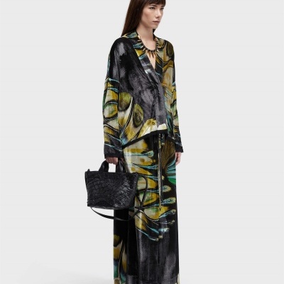 Mulher com roupa de padrão abstrato colorido e mala preta em fundo branco.