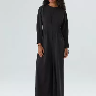 Mulher com macacão preto de manga comprida, óculos de sol brancos e sandálias brancas