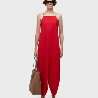 Macacão vermelho feminino com alças finas, mala e óculos escuros.