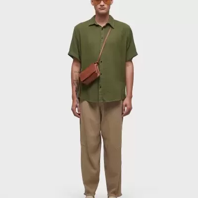 Homem com camisa verde, calças castanhas e óculos de sol laranja